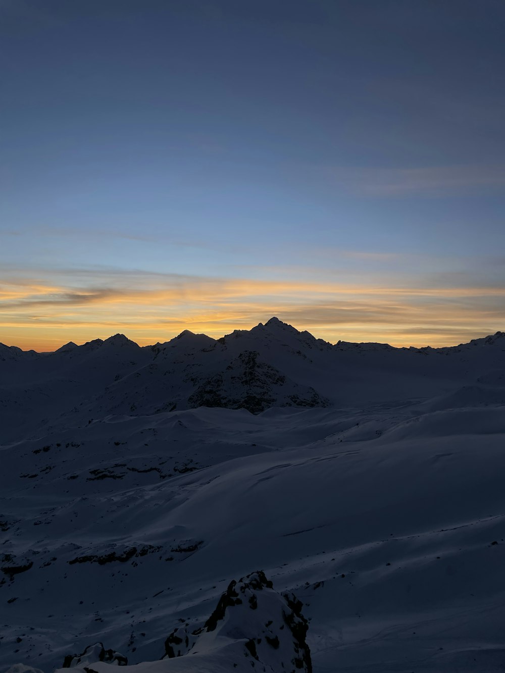 the sun is setting over a snowy mountain range