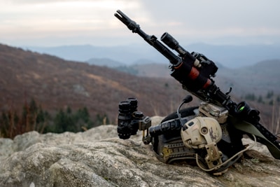 Airsoft replicas and original military items displayed outdoors on rugged terrain.