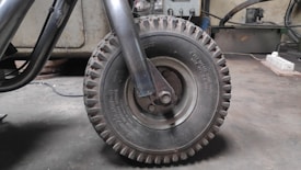 A close-up view of a large, rugged industrial rubber wheel attached to a metal frame. The environment appears to be a workshop or garage, with various tools and machinery visible in the background.