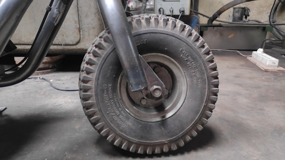 A close-up view of a large, rugged industrial rubber wheel attached to a metal frame. The environment appears to be a workshop or garage, with various tools and machinery visible in the background.