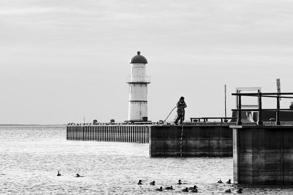 a black and white photo of a man standing on a pier next to a light