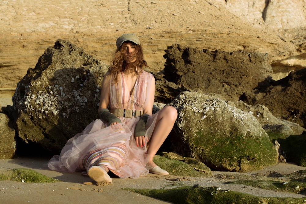 a woman in a pink dress sitting on a rock