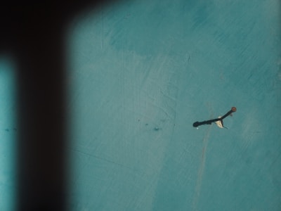 A single rusty nail protrudes from a teal-colored surface, casting a long shadow across the textured background. A hint of paper or a similar material is caught on the nail, adding to the scene.