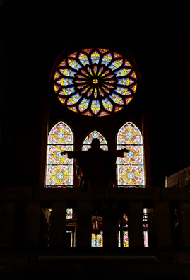 A silhouette of the artist against a stained glass window casting colorful patterns.