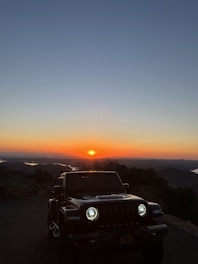 A sleek armored Land Cruiser 300 parked on a rugged terrain at sunset.