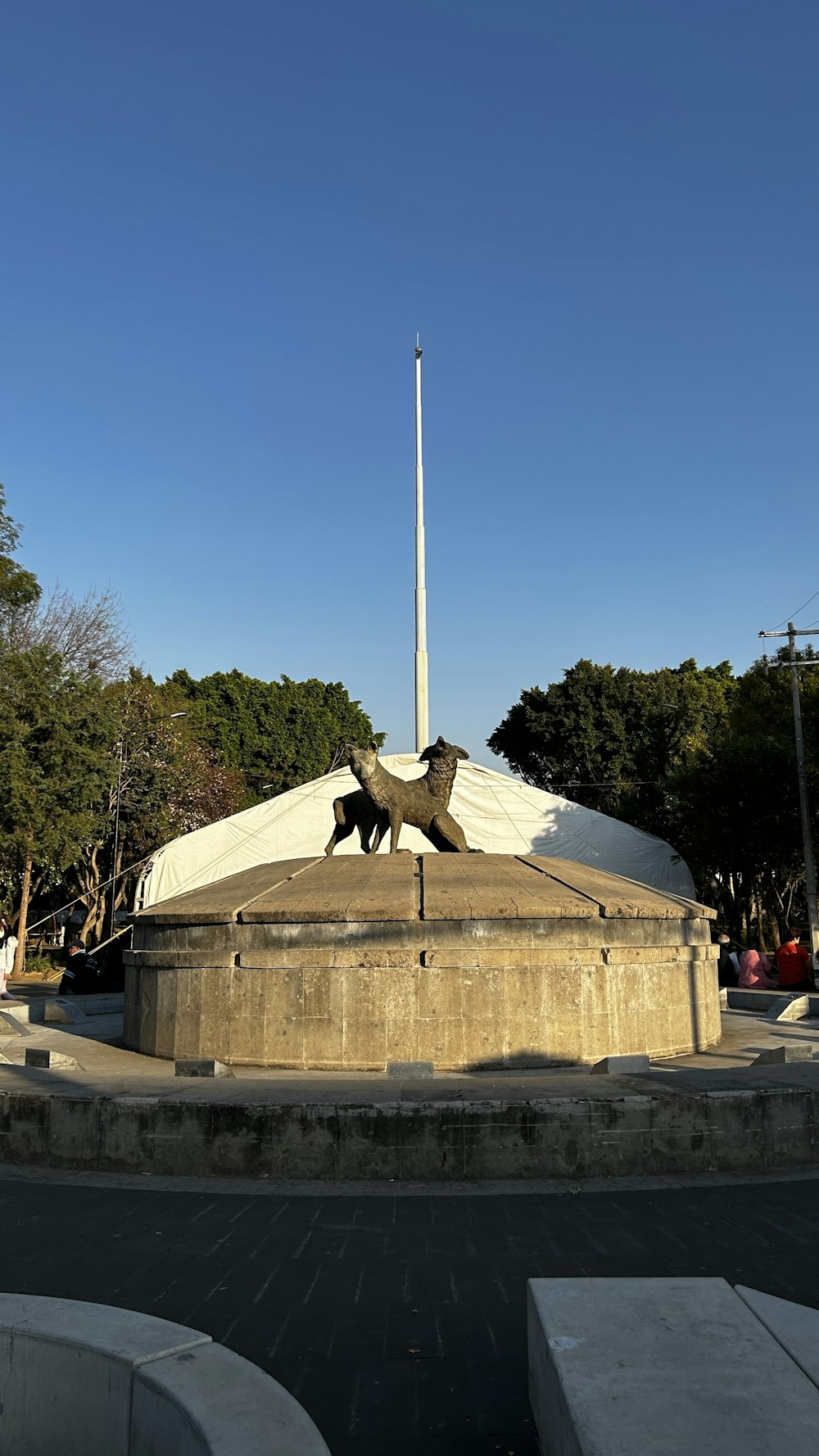 Une statue de deux chiens devant un mât de drapeau