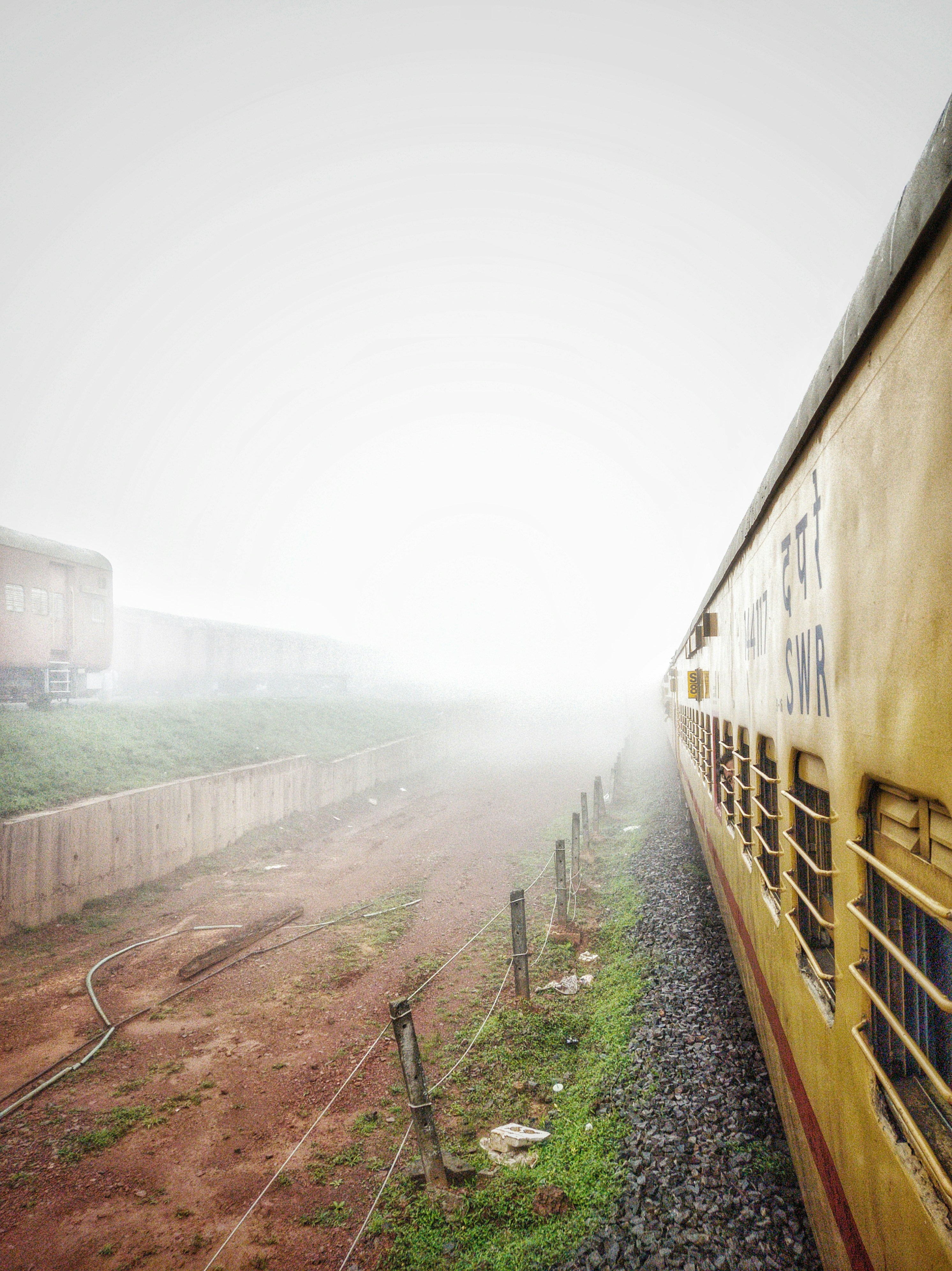 Un tren amarillo que viaja por las vías del tren junto a un campo