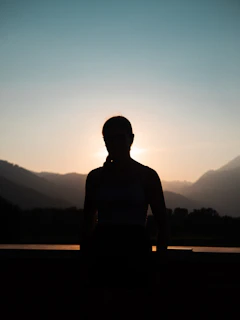 Silhouette of a mestizo athlete standing on a ridge with Cotopaxi volcano and soft orange dawn light.