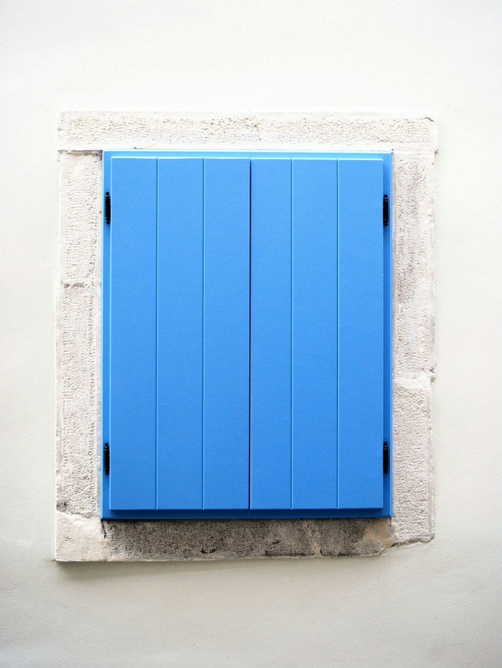 a blue shuttered window on a white wall