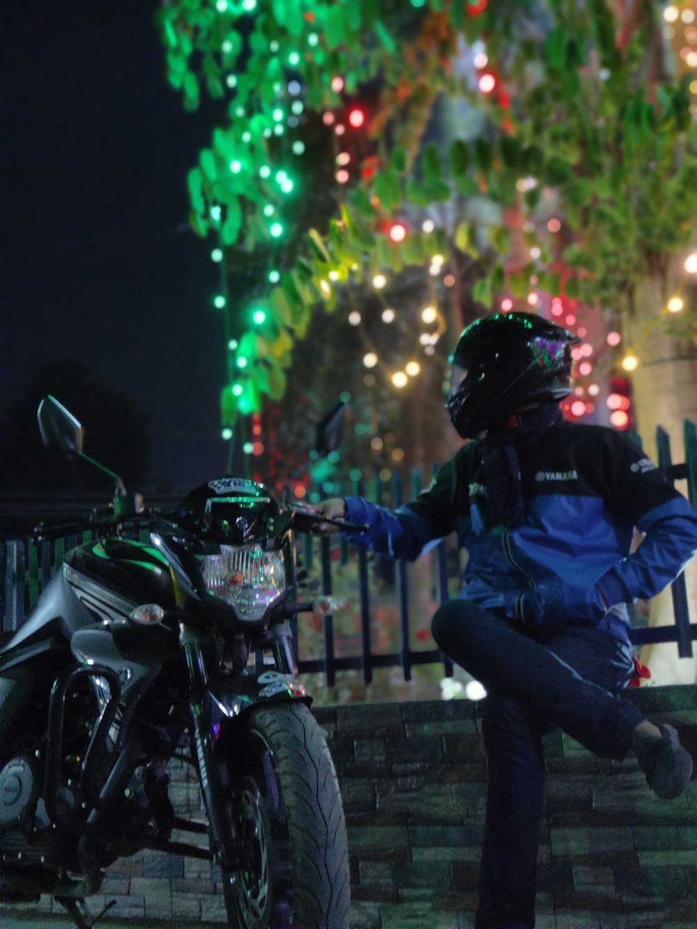 a person sitting on a motorcycle in front of a fence