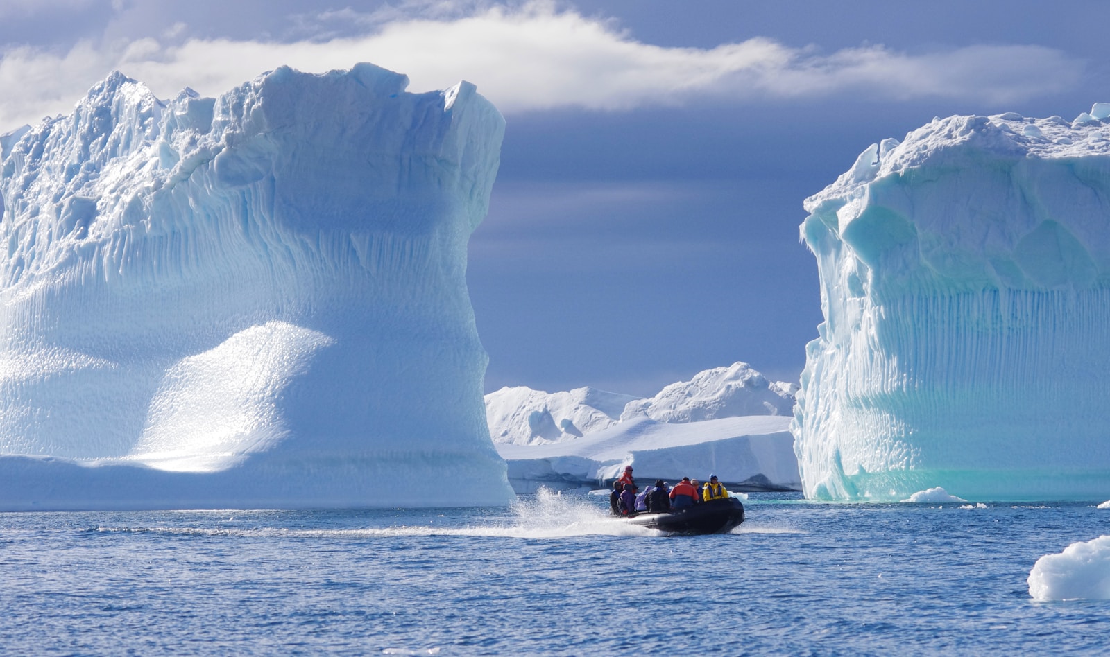 A zodiac carrying a group of passengers speeding between two enormous blue-white icebergs