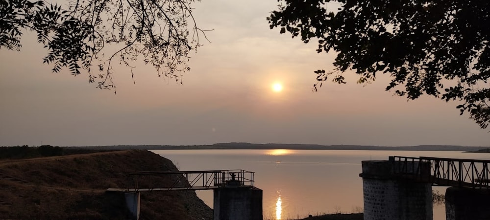 a sunset over a body of water with a bridge in the foreground