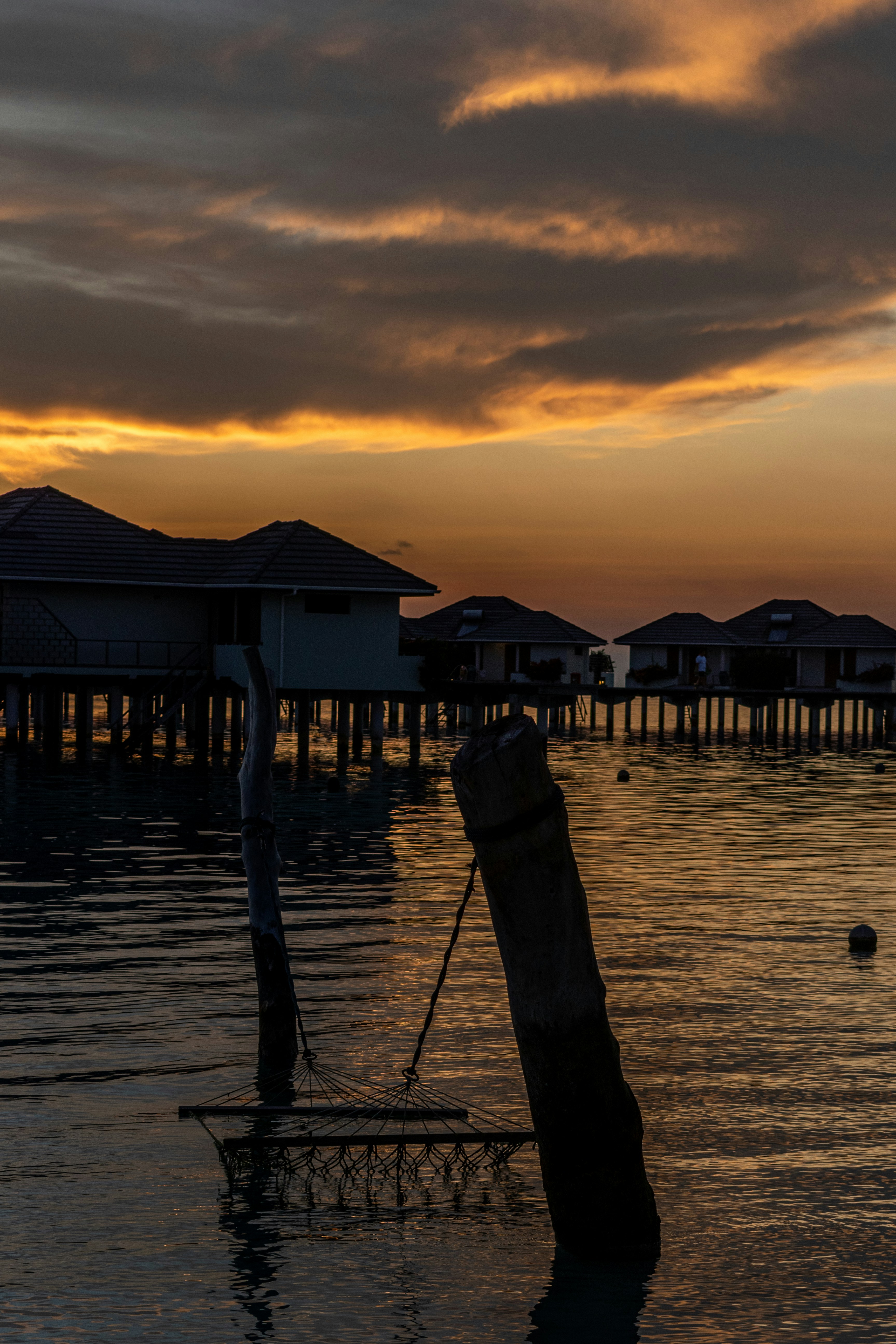 Luxury overwater bungalow at Maldives resort at golden hour, warm amber light on thatched roof, calm turquoise water below, dark deep ocean horizon