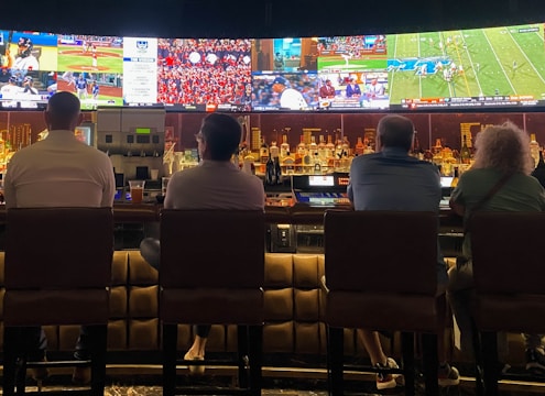 A group of friends watching a live sports game on a large screen TV, cheering enthusiastically.