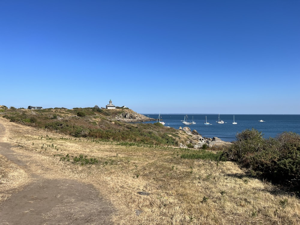 a dirt path leading to a beach with sailboats in the water