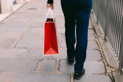 a man walking down a sidewalk carrying a red bag