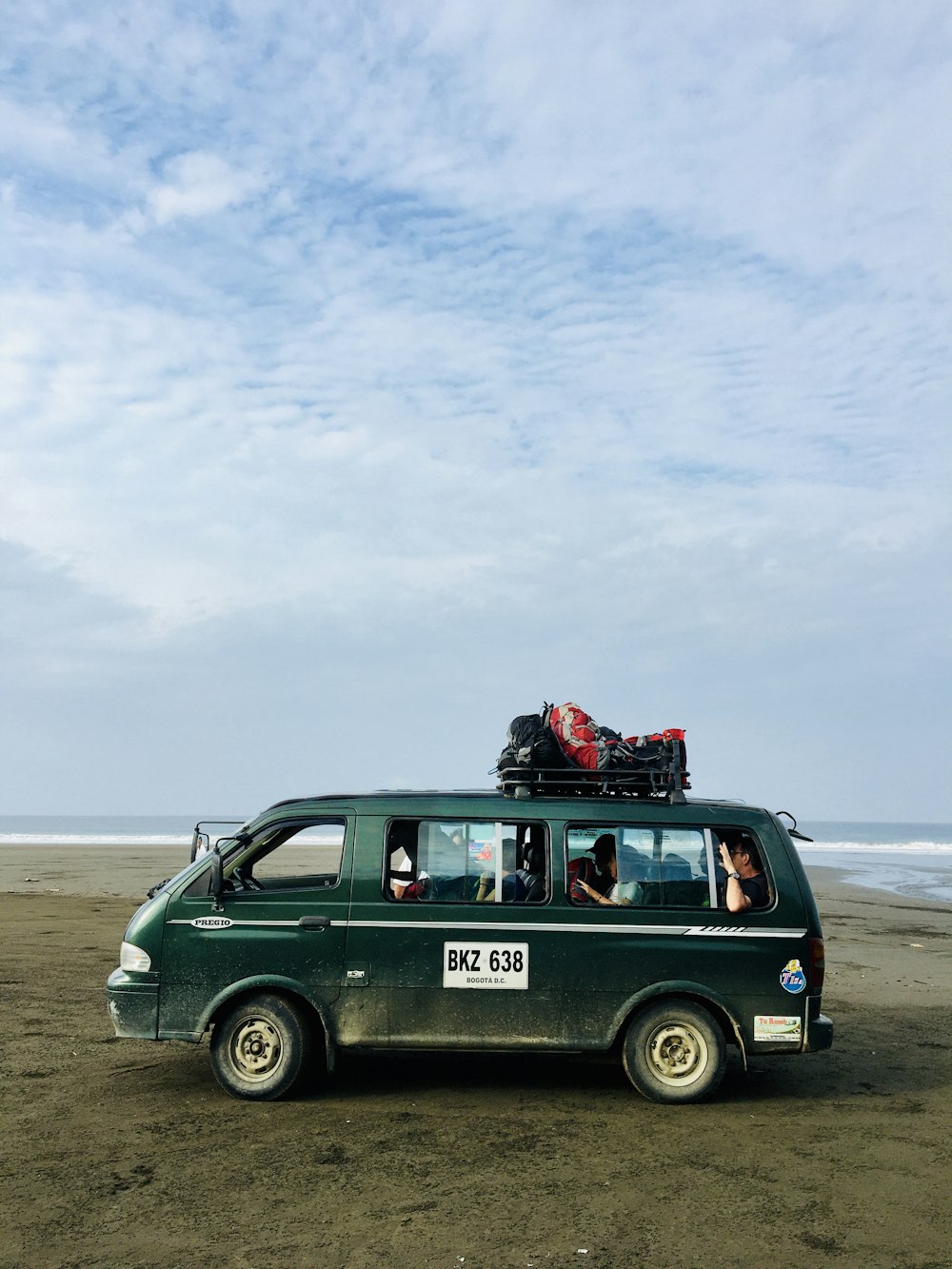 a van is parked on the beach with luggage on top