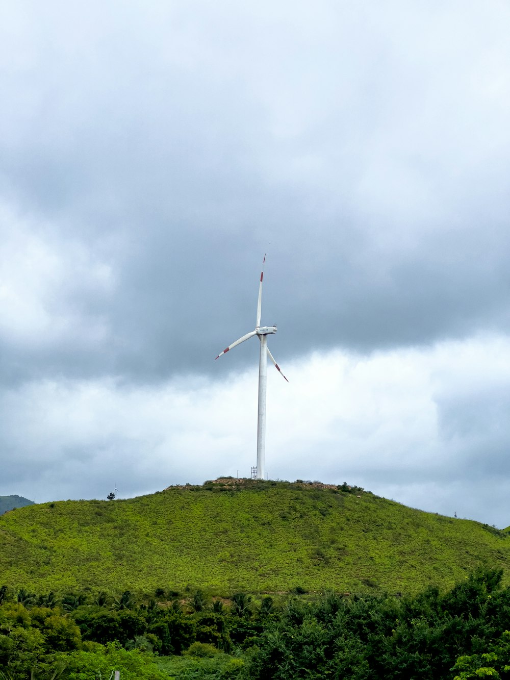 a wind turbine sitting on top of a lush green hillside