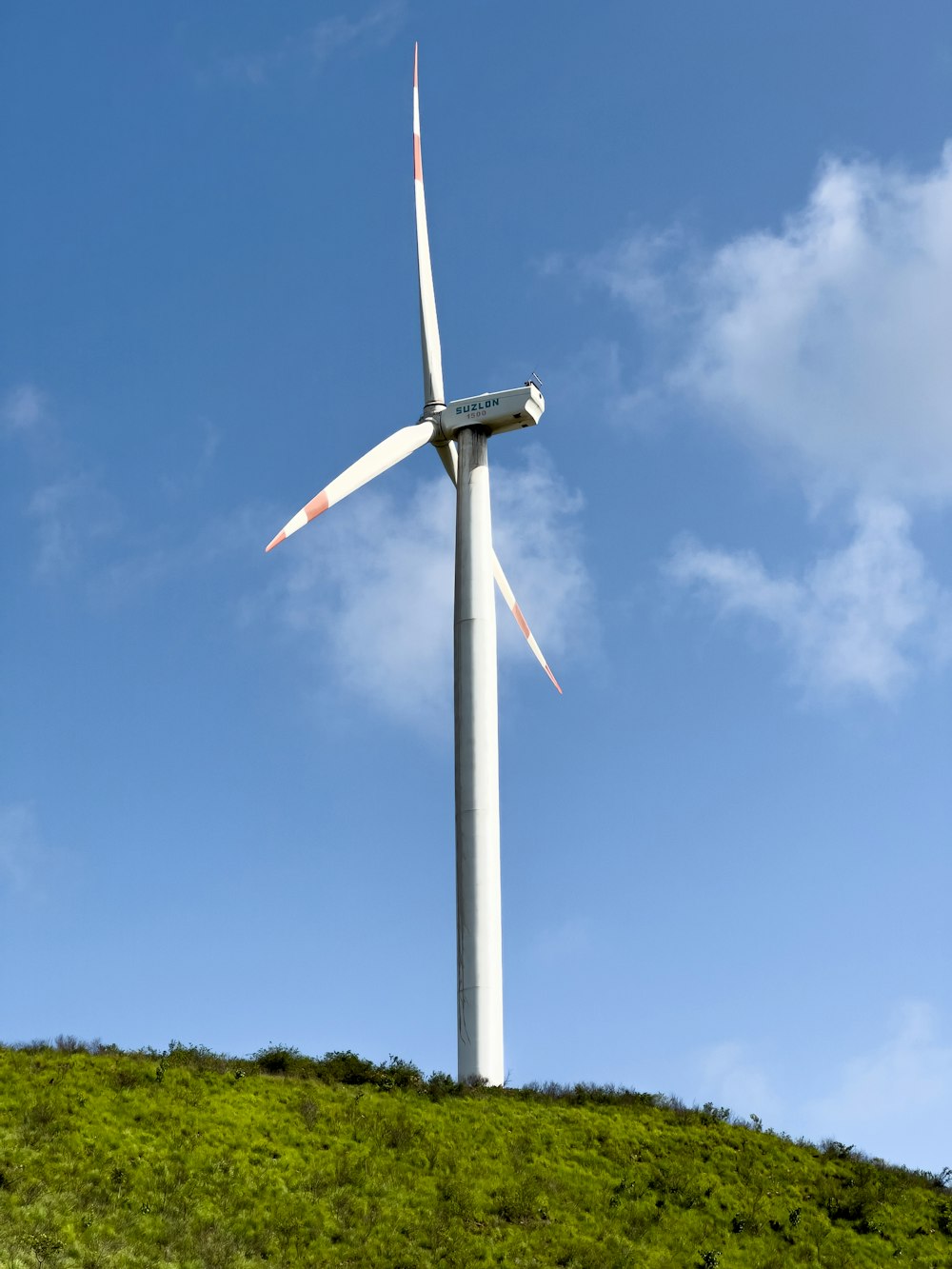 a wind turbine sitting on top of a lush green hillside