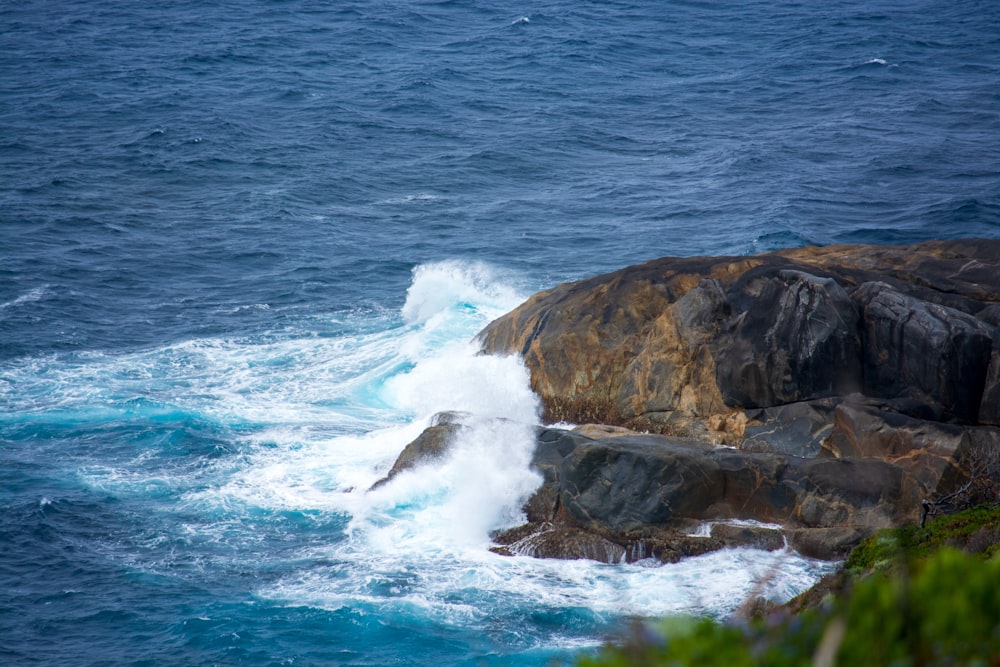 a wave crashes into the rocks near the ocean