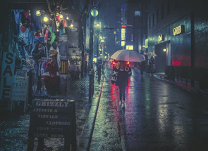 Wide shot of a group of friends in layered streetwear standing under a glowing streetlamp on a rainy street.