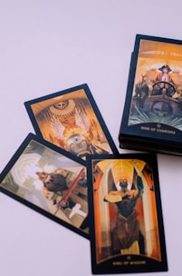 A set of tarot cards is laid out on a light surface. The cards feature illustrated designs with rich colors and intricate details. They depict various figures and symbols, including a person steering a ship, an angelic figure with wings, and a figure holding a disc, suggesting roles or personalities.