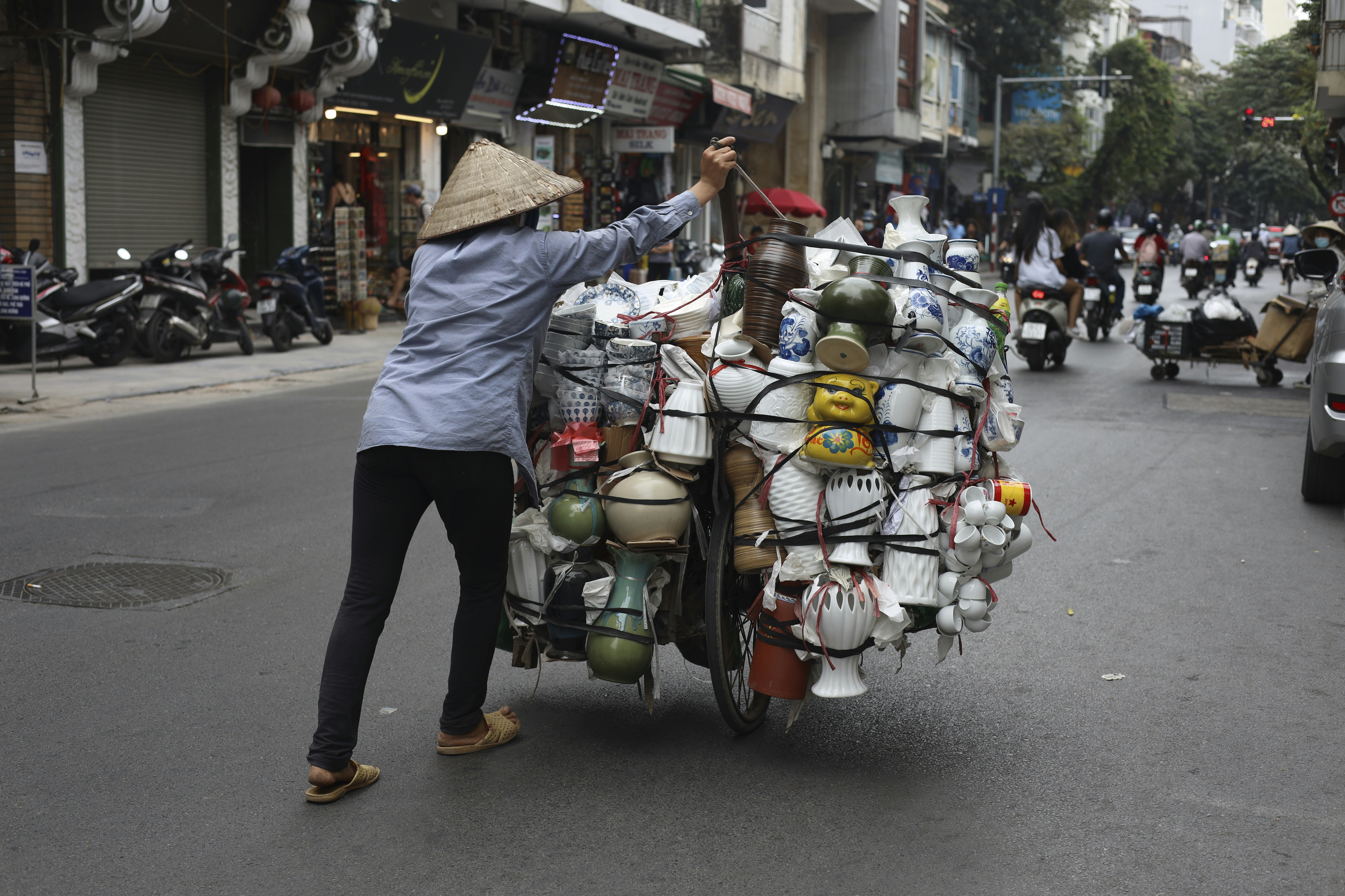 a woman pushing a cart full of items down a street