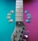 A guitar neck lies diagonally across a colorful background split into teal and magenta sections. Guitar picks in various shades of blue and beige are arranged on both sides of the neck.