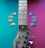 A guitar neck lies diagonally across a colorful background split into teal and magenta sections. Guitar picks in various shades of blue and beige are arranged on both sides of the neck.
