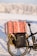 A bicycle equipped with a large wrapped gift box on the rear rack, set against a snowy winter landscape. The gift box features a red wrapping with white and blue motifs. A black pannier is attached to the bike, adorned with a small evergreen branch and a red and white striped ribbon. The tire tracks in the snow and a blurred line of snow-covered trees in the background add to the festive, winter theme.