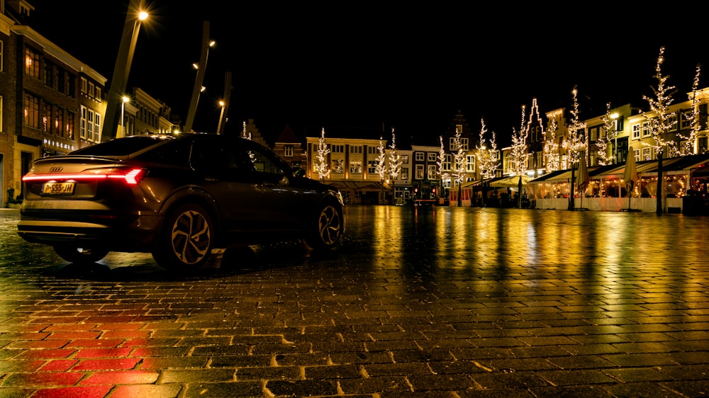 a car is parked on a cobblestone street at night