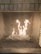 A fireplace with visible flames burning on a bed of dark, shiny stones inside a mesh enclosure. The background consists of brickwork, adding a rustic feel.
