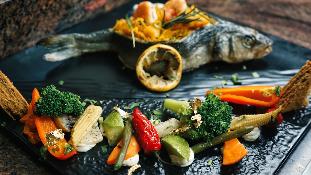 a black plate topped with fish and veggies