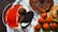 A dessert spread featuring a glass of creamy pudding topped with a vibrant red sauce, chocolate truffles, and a black sandwich cookie. Surrounding the glass are various other desserts, including a chocolate-drizzled pastry and some small orange-hued balls.