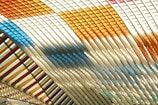 An abstract pattern featuring intersecting curved lines in various colors including orange, yellow, blue, and white. The lines are arranged in a way that creates a sense of movement and depth, resembling a woven textile or architectural design.