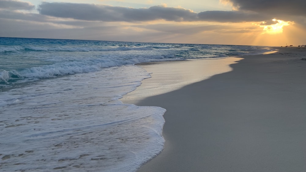 the sun is setting over the ocean on the beach