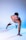 A man is performing a one-armed push-up in a studio with a blue and white gradient background. He is wearing white athletic shorts and has a focused expression on his face.