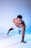 A man is performing a one-armed push-up in a studio with a blue and white gradient background. He is wearing white athletic shorts and has a focused expression on his face.