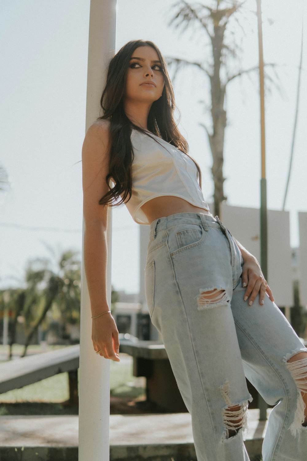 a woman leaning against a pole wearing ripped jeans
