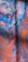 Abstract artwork featuring swirling patterns of vibrant colors including deep blues, fiery oranges, and splashes of red. The surface displays a marbled effect with intricate textures resembling bubbles or foam near the top.