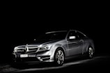 A silver luxury car is set against a dark background, highlighted dramatically by focused lighting that emphasizes its sleek and shiny bodywork.