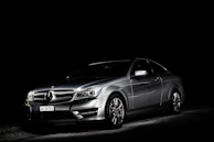 Side profile of a silver luxury car with satin finish and carbon fiber accents under soft white lighting.