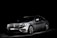 A silver luxury car is set against a dark background, highlighted dramatically by focused lighting that emphasizes its sleek and shiny bodywork.