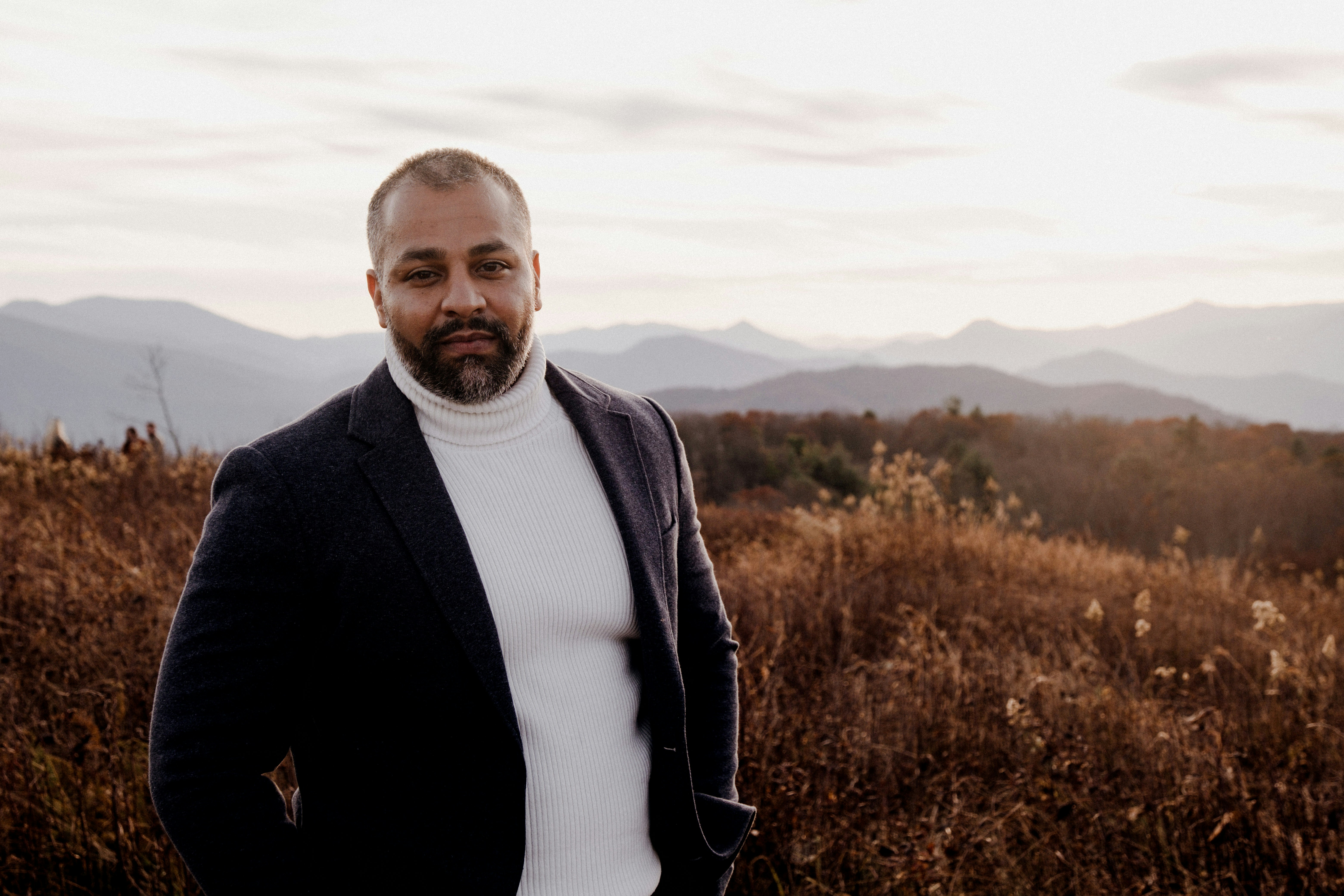a man standing in a field with mountains in the background