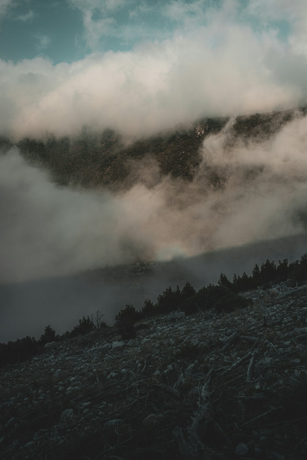 a mountain covered in fog and clouds under a blue sky