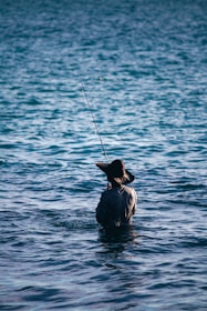 An angler wearing a 50x50 Outdoors hat, casting a line into a calm Texas bay at sunrise.
