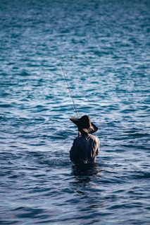 An angler wearing a 50x50 Outdoors hat, casting a line into a calm Texas bay at sunrise.