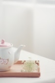 A minimalist ceramic teapot with soft steam rising, set on a wooden tray.