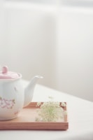 A delicate porcelain teapot releasing gentle steam on a bamboo mat under soft natural light.