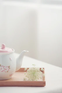 A peaceful morning setup with a ceramic teapot and cup on a wooden tray surrounded by fresh flowers